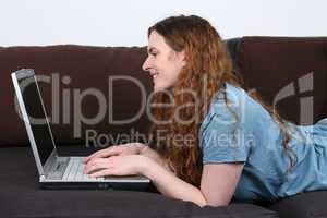 Junge Frau liegt auf Sofa und benutzt Laptop Computer