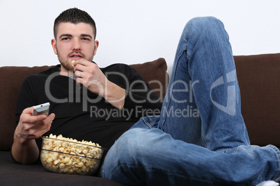 Junger Mann schaut fernsehen und isst Popcorn