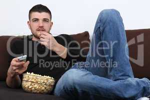 Junger Mann schaut fernsehen und isst Popcorn