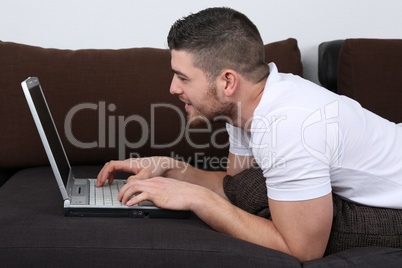 Junger Mann liegt auf Sofa und benutzt Laptop Computer