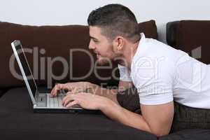 Junger Mann liegt auf Sofa und benutzt Laptop Computer