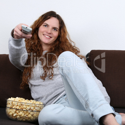 Junge Frau schaut fernsehen und isst Popcorn