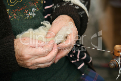 The hands of the elderly woman spinning a wool.