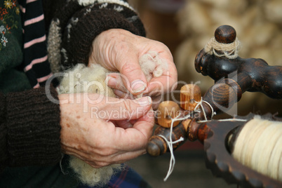 The hands of the elderly woman spinning a wool.