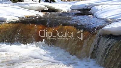 A clear water flowing between the snow-covered are a
