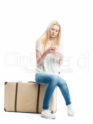 Blonder Teenager mit Koffer simst mit Handy