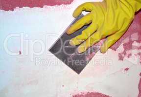 Gloved hand sanding old paint on a wall
