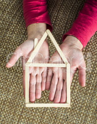 hands holding model house made of wooden sticks