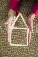 hands holding model house made of wooden sticks