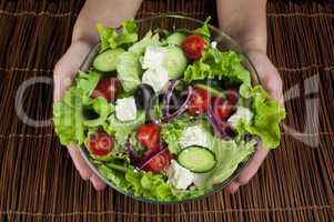 hands holding salad in a glass bowl