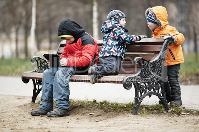 three young boys playing on a park bench in winter