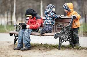 three young boys playing on a park bench in winter