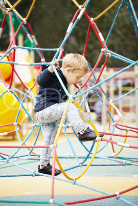 happy little boy climbing on playground equipment