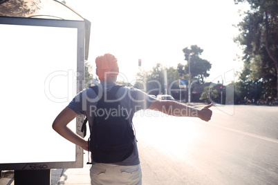 man standing near bus stop thumbing a lift
