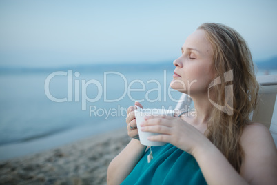 woman with closed eyes enjoying a cup of tea at the seaside