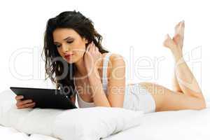 young woman reading a tablet on her bed