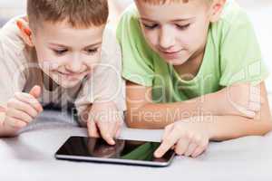 Two smiling child boys playing games or surfing internet on tabl