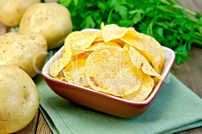 Chips in a bowl with a potato on the board and napkin