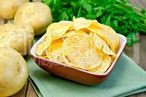 Chips in a bowl with a potato on the board and napkin