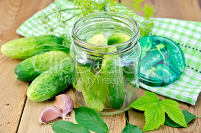 Cucumbers in jar with leaves and napkin on the board