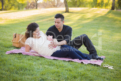Pregnant Hispanic Couple with Piggy Bank on Belly in Park