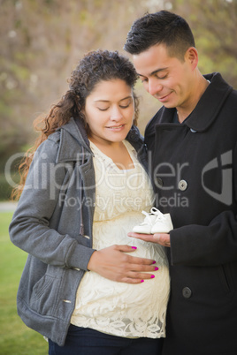 Hispanic Pregnant Couple Holding Baby Shoes Outside