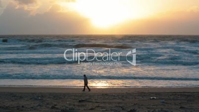 Man walking on the beach with storm waves at sunset