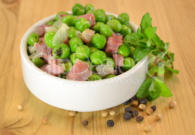 Peas cooked with ham and herbs on a white bowl