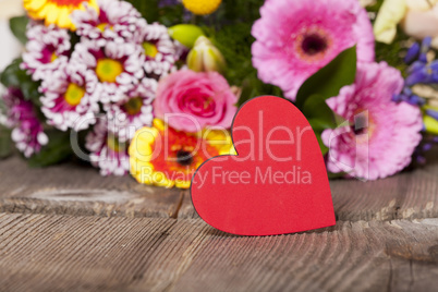 rotes herz mit buntem blumenstrauß im hintergrund