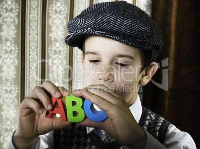 Child in vintage clothes hold letters a b c