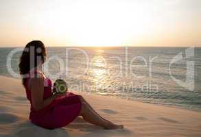 Junge hübsche Frau sitzt auf Düne am Meer - Sonnenuntergang