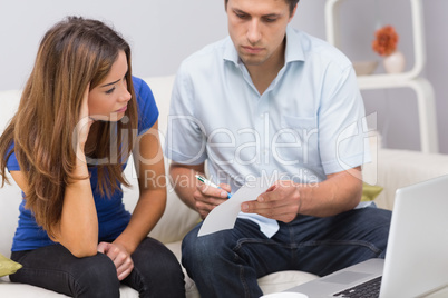 Worried couple paying bills online with laptop at home
