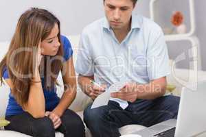 Worried couple paying bills online with laptop at home