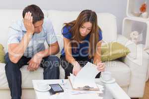 Worried couple paying their bills in living room at home