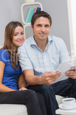 Smiling couple with bills in living room at home