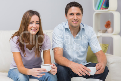 Cute couple sitting on sofa with tea cups at home