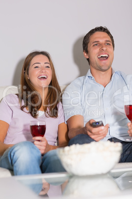 Happy couple with wine and popcorn enjoying a movie at home