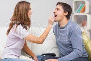 Young cheerful woman feeding popcorn to man on sofa