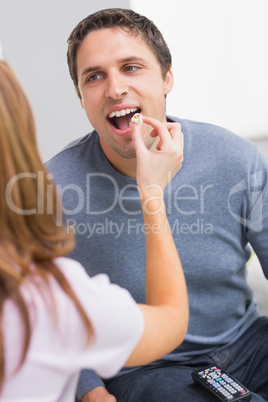 Cropped woman feeding popcorn to a happy man at home