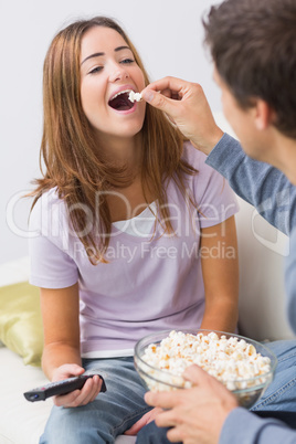 Cropped man feeding popcorn to a happy woman at home