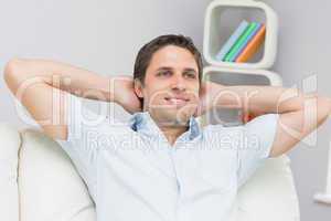 Thoughtful man sitting with hands behind head in the living room