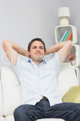 Thoughtful man sitting with hands behind head in the living room