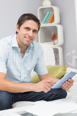 Smiling man with bills using digital tablet in the living room