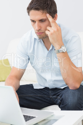 Serious young man using laptop in living room