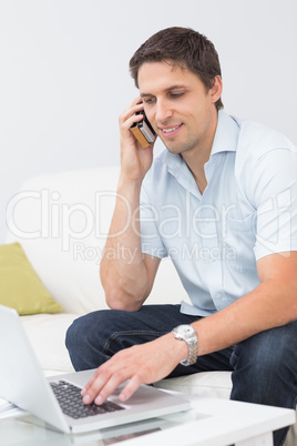 Smiling man using laptop and cellphone in the living room