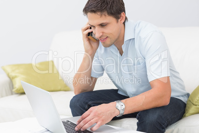 Smiling man using laptop and cellphone in living room