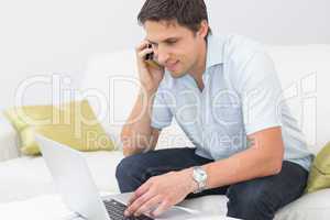 Smiling man using laptop and cellphone in living room