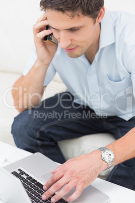 Young man using laptop and cellphone at home