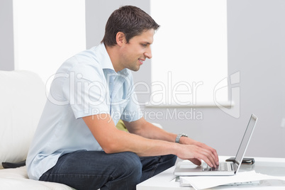 Side view of smiling man using laptop at home