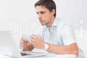 Serious man with teacup using laptop at home